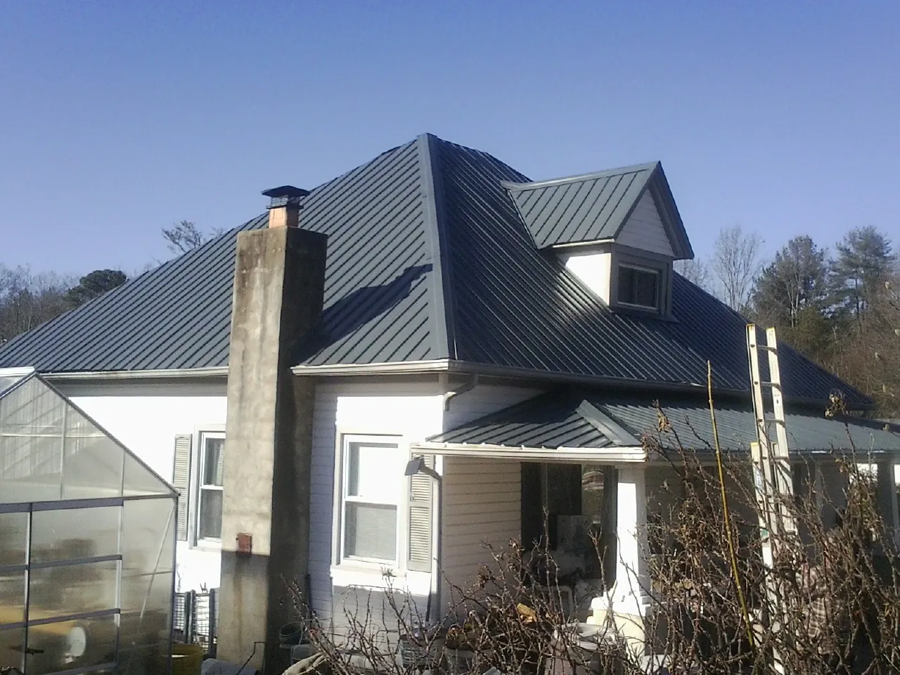 Dark blue standing seam metal roof on a white farmhouse with dormer — Slate & Tile Roof Repair by Roofing Brothers in Miltona