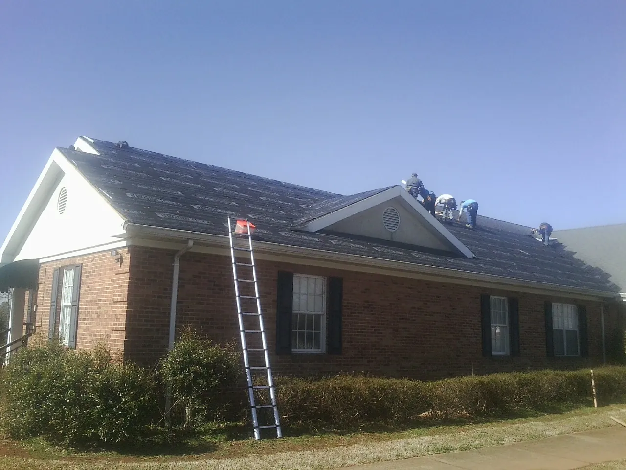 Crew tearing shingles off a brick ranch roof with a ladder set — Emergency Roof Repair work by our crew in Miltona