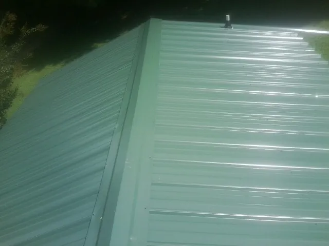 New green metal panels meeting at the ridge of a roof — Flat Roof Repair work by our crew in Miltona