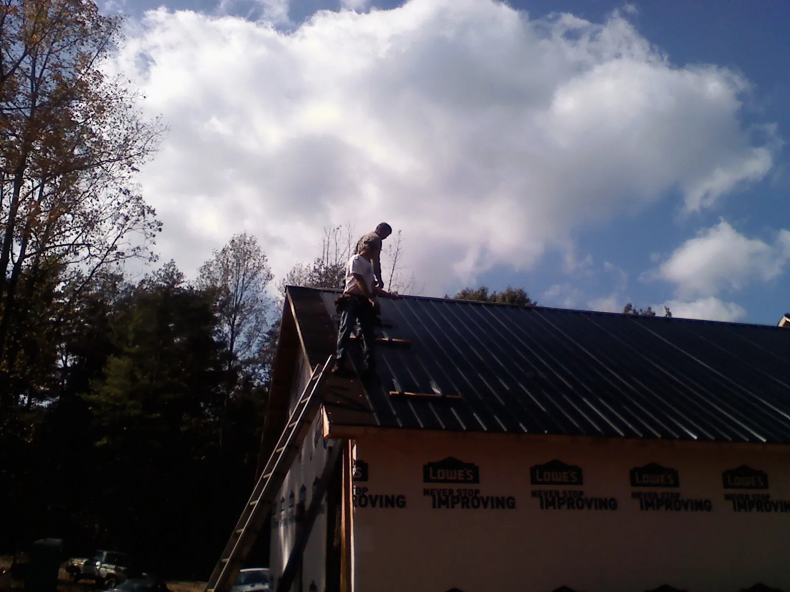 Roofer fastening dark metal panels high against a cloudy sky, from a Roof Inspection job in Miltona